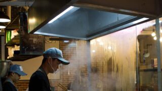 A cook prepares traditional Chinese noodles in a bustling Shanghai street food stall.